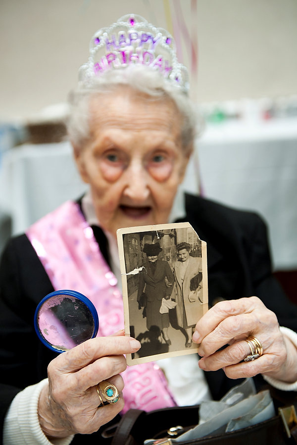 The staff of The Atrium at Hamilton Park in Jersey City throws a birthday party on Friday, April 11, 2014, for Alice Mospak who will turn 105 years old on Sunday. Here, Alice Mospak shows a photo she keeps in her purse of herself, right, and her mother walking down Fifth Avenue in New York City on the day they arrived in the United States from Estonia in 1951. She uses a magnifying glass to  help her read. (Reena Rose Sibayan /The Jersey Journal)