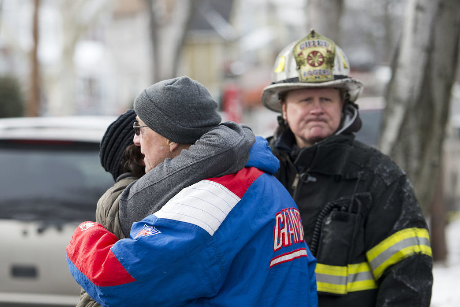 Neighbors comfort each other as firefighters battle a five-alarm blaze that ripped through two attached homes in Bayonne at 12 and 14 West 34th St. on Monday, Feb. 16, 2015. At right is Fire Chief Gregory Rogers. Reena Rose Sibayan | The Jersey Journal