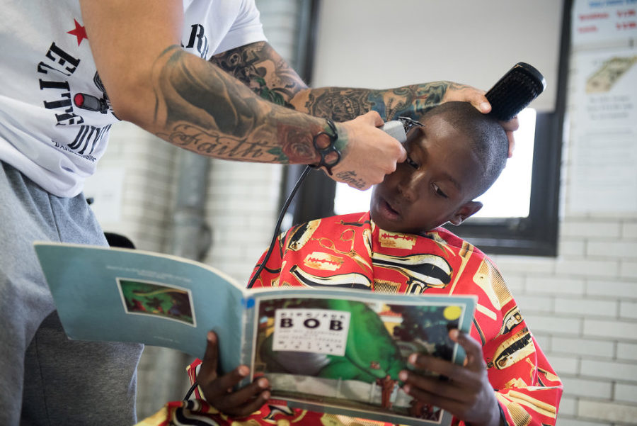 Micah Jones, 11, who will be entering fifth grade, reads aloud the book "Dinosaur Bob and His Adventures with the Family Lazardo" to barber Abraham Castillo of The Booth Barbershop, during the Books & Clips free back-to-school haircuts event organized by the Dr. Ercel F. Webb Elementary School (School 22) in Jersey City for its students on Monday, Aug. 31, 2015. Reena Rose Sibayan | The Jersey Journal