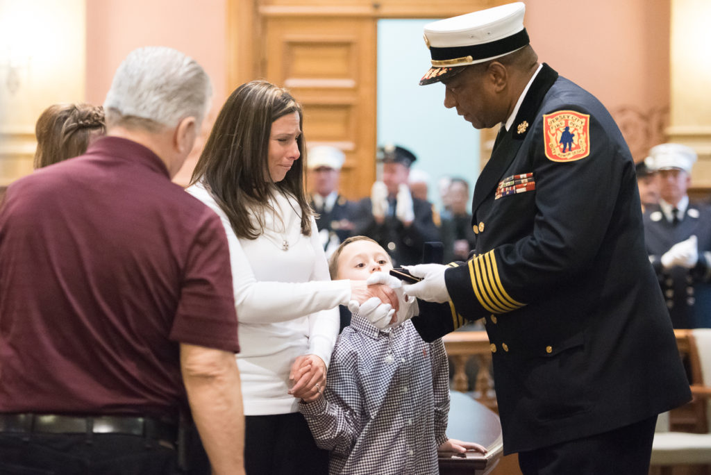 The Jersey City Fire Department promoted 11 firefighters to the rank of fire captain, including the city's first Filipino-American fire captain, and two fire captains to the rank of battalion chief during a ceremony at City Hall on Friday, Dec. 11, 2015. Fallen Firefighter James Woods was also posthumously promoted to the rank of fire captain. Here, Fire Chief Darren Rivers presents Woods' family with his captain's badge. Reena Rose Sibayan | The Jersey Journal