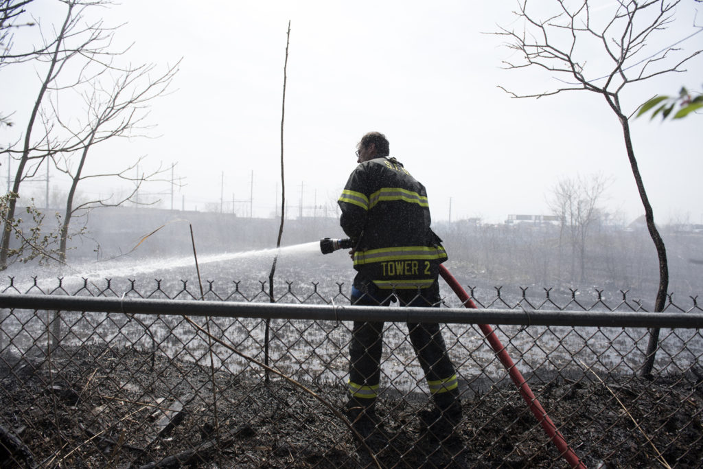 A Secaucus firefighter puts out hotspots at the foot of Henry Street in Secaucus after a brush fire broke out on Tuesday, April 19, 2016. Reena Rose Sibayan | For The Jersey Journal